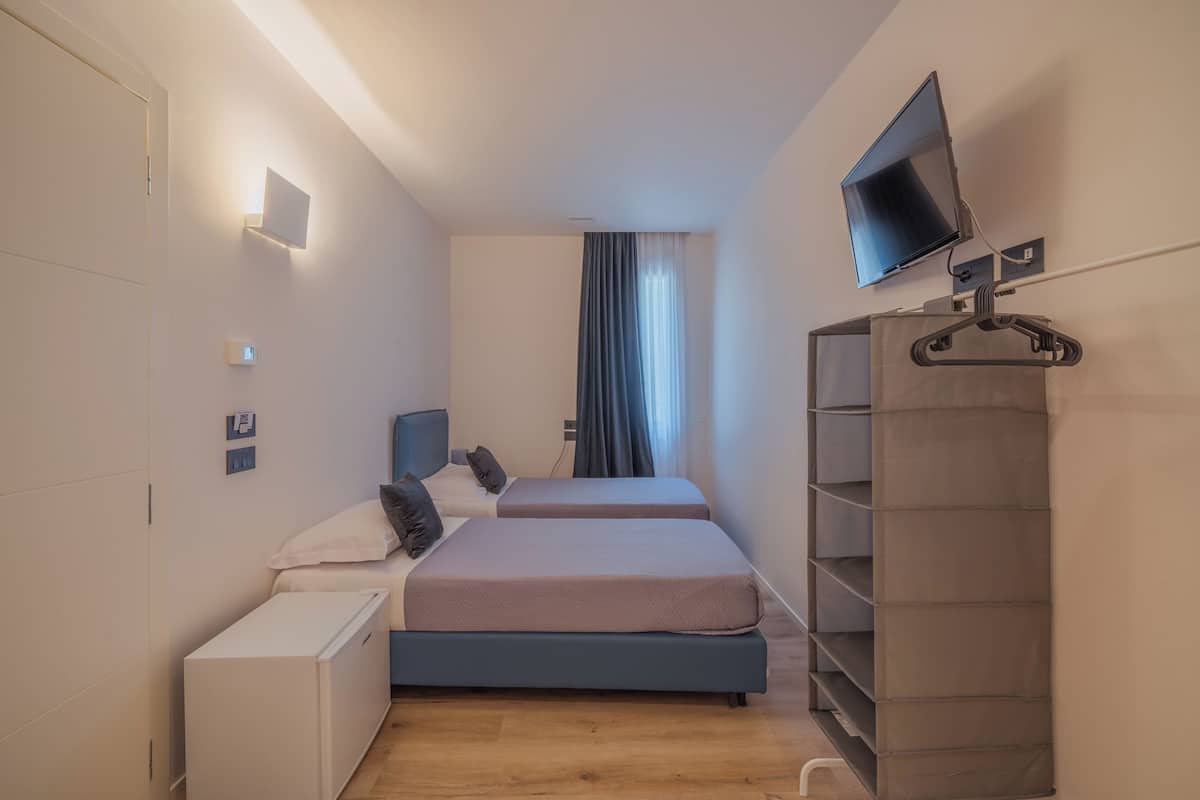 A bedroom with two beds, a TV, a wardrobe, and a bedside table.