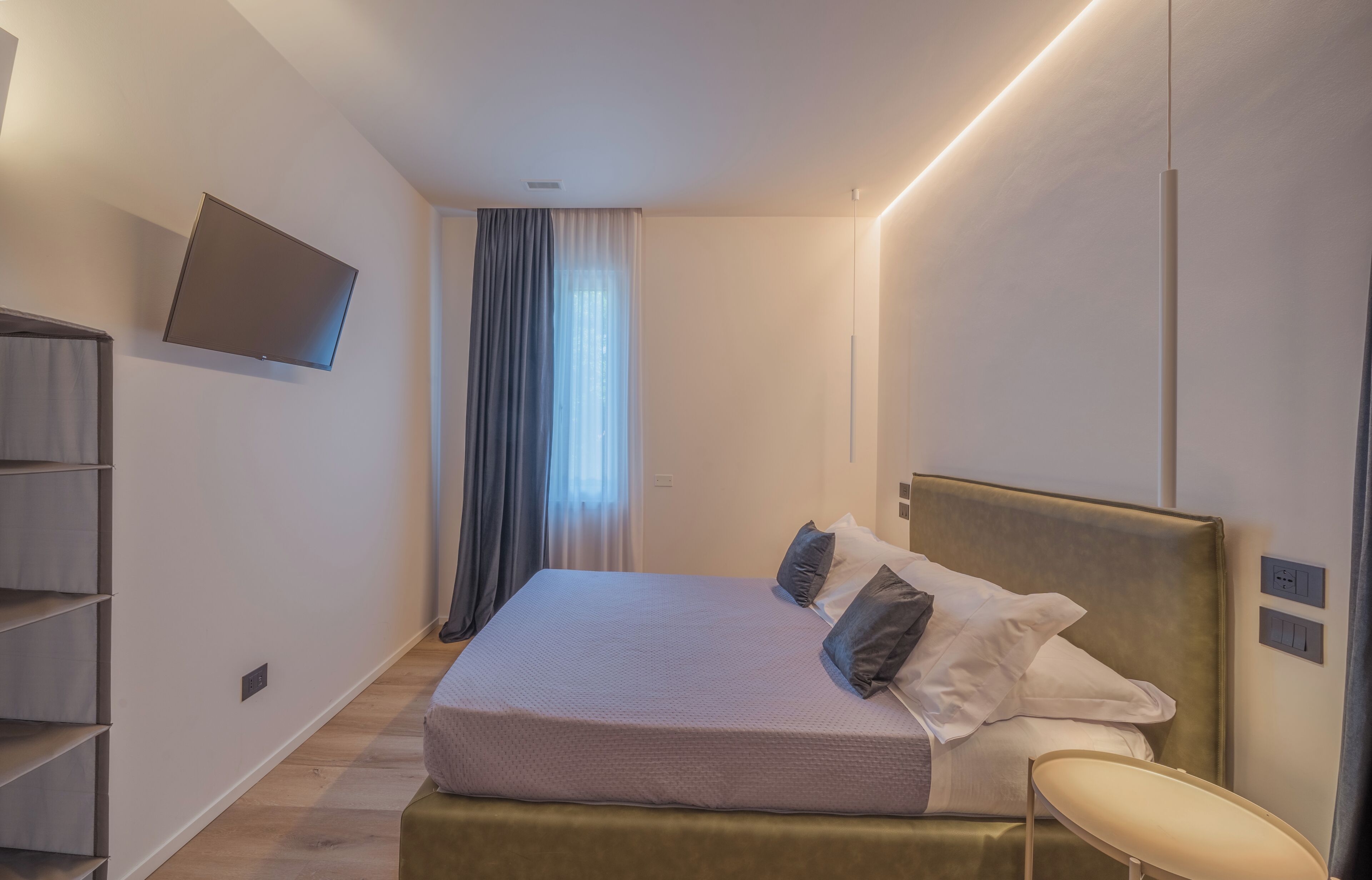 Habitació d'hotel moderna amb un llit, una televisió penjada a la paret, una taula de nit i un moble prestatge integrat.