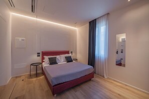 A modern hotel room with a red bed, a small bedside table, a wall-mounted air conditioner, and a window with curtains.