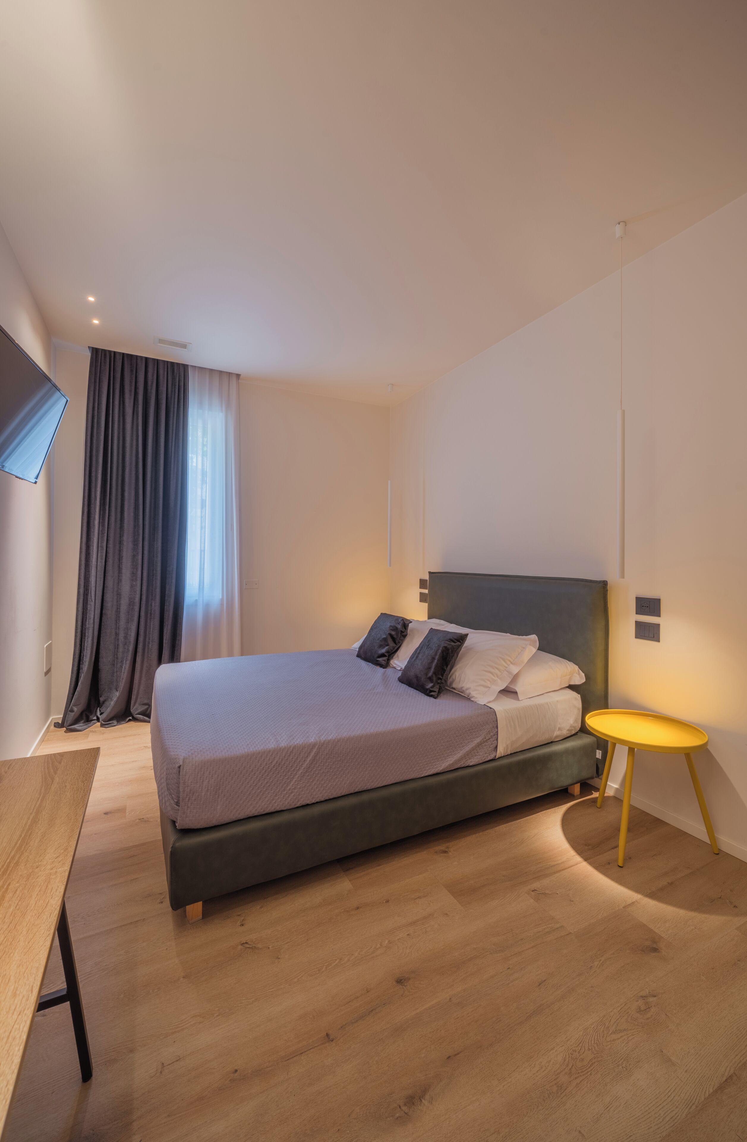 Et moderne soveværelse med seng, natbord, lampe og et vindue med gardiner.
