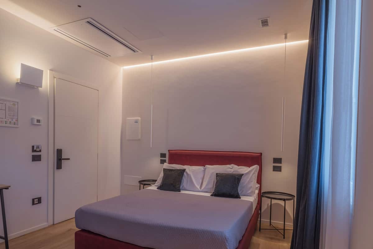 A modern bedroom with a red bed, wooden flooring, and a door with a handle.