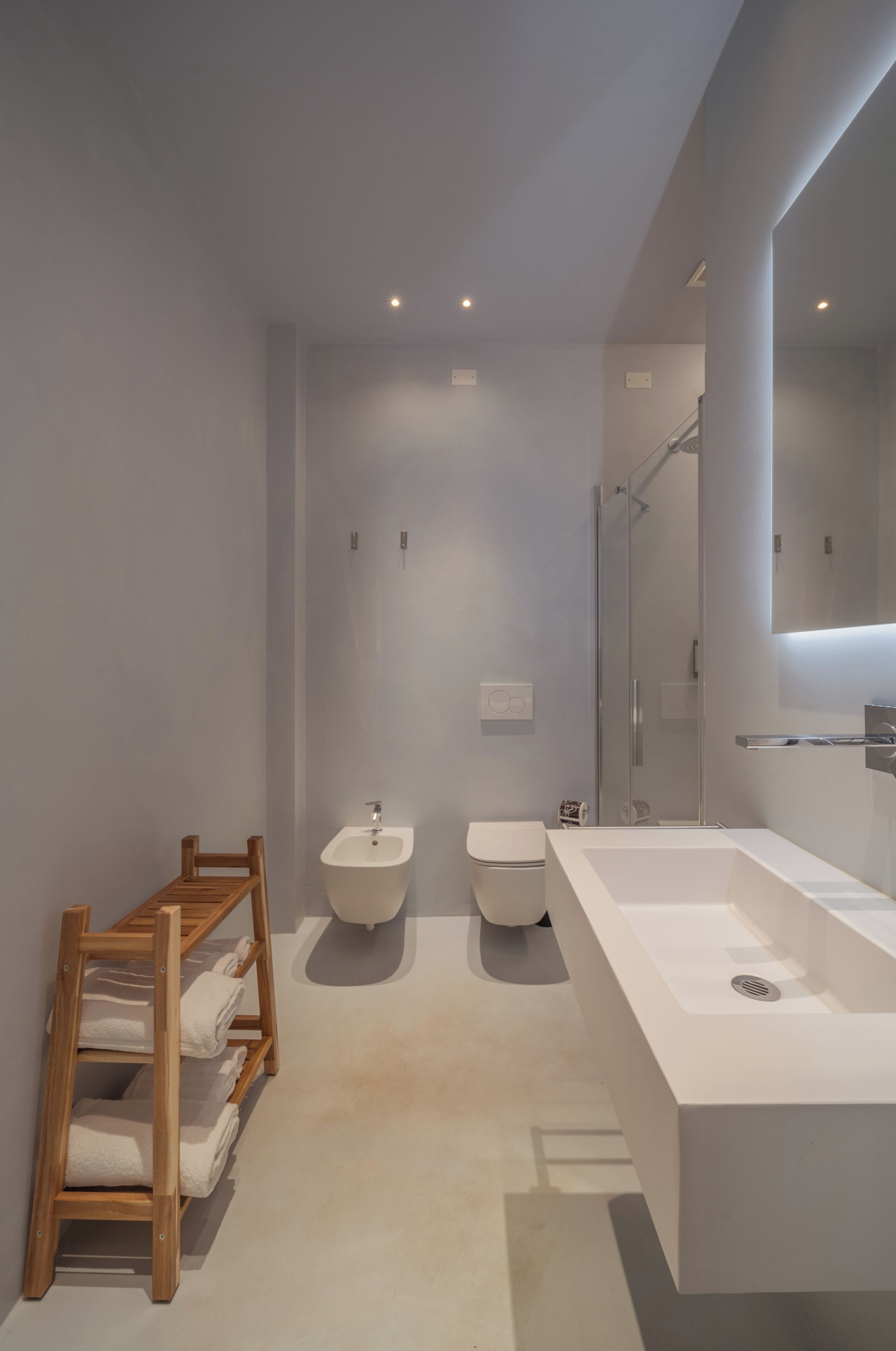 Een moderne badkamer met een groot wit wastafelmeubel, een douche en een houten handdoekhouder.