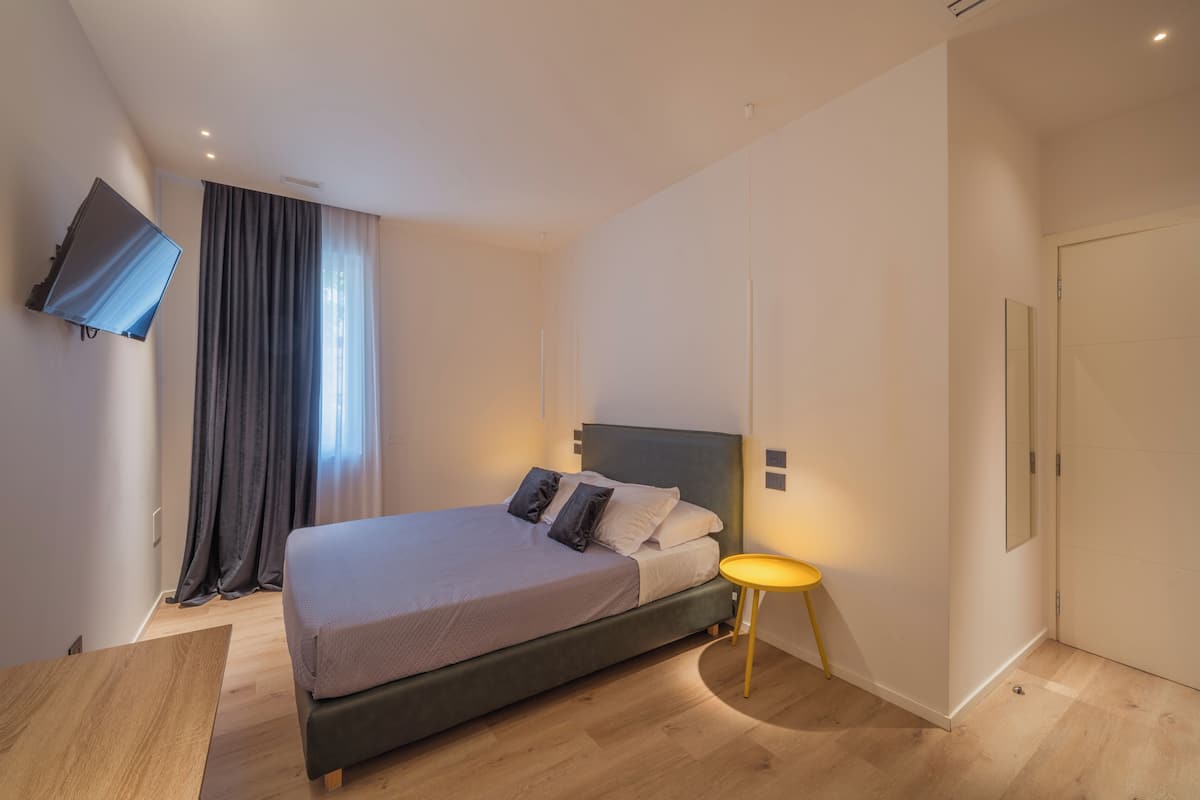 A bedroom with a bed, a TV mounted on the wall, a bedside table, and a door.