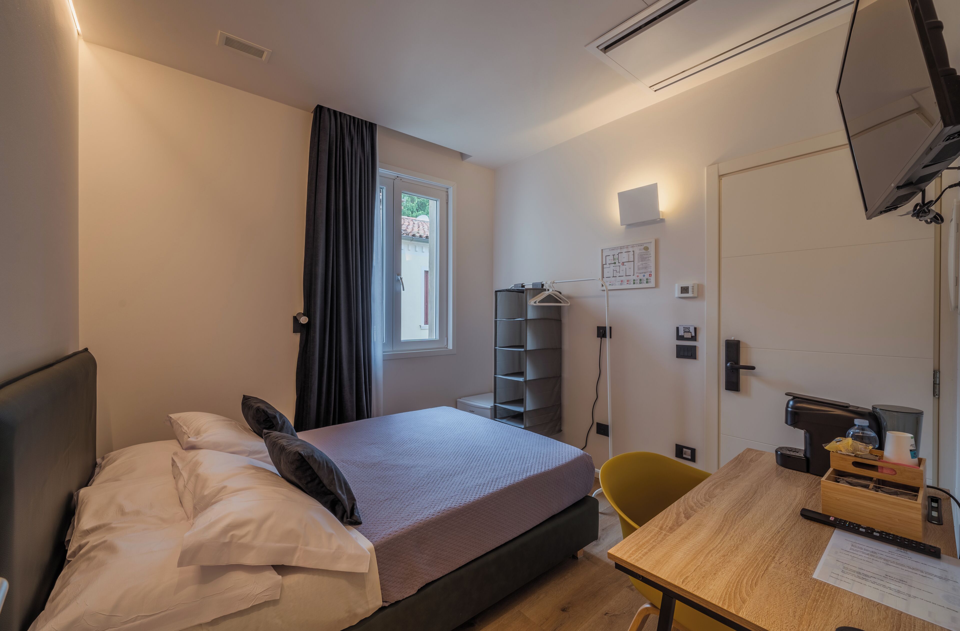 Habitación de hotel con cama, escritorio, silla, armario, ventana con cortinas y puerta.