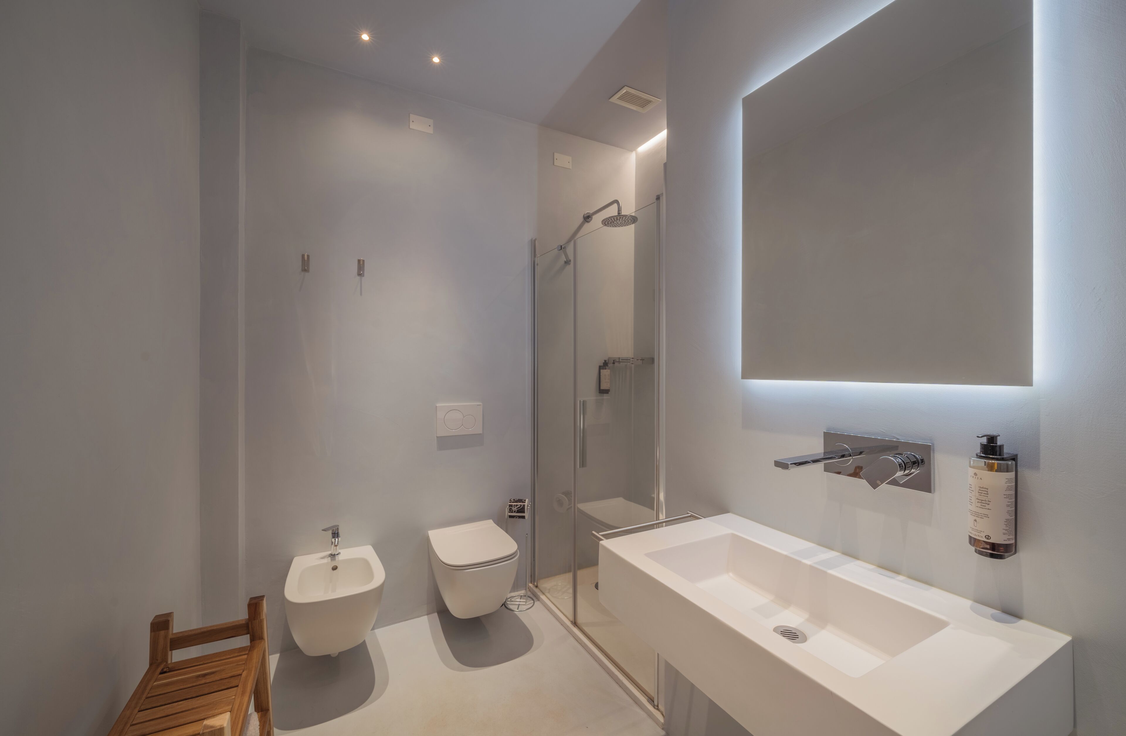 A modern bathroom with a large mirror, a shower, a bidet, and a sink.