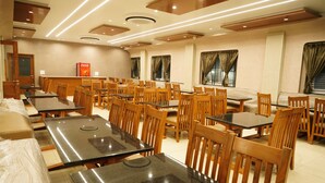 Un grand espace dédié à la salle à manger, avec plusieurs tables et chaises, un réfrigérateur Coca-Cola et une grande fenêtre agrémentée de rideaux.