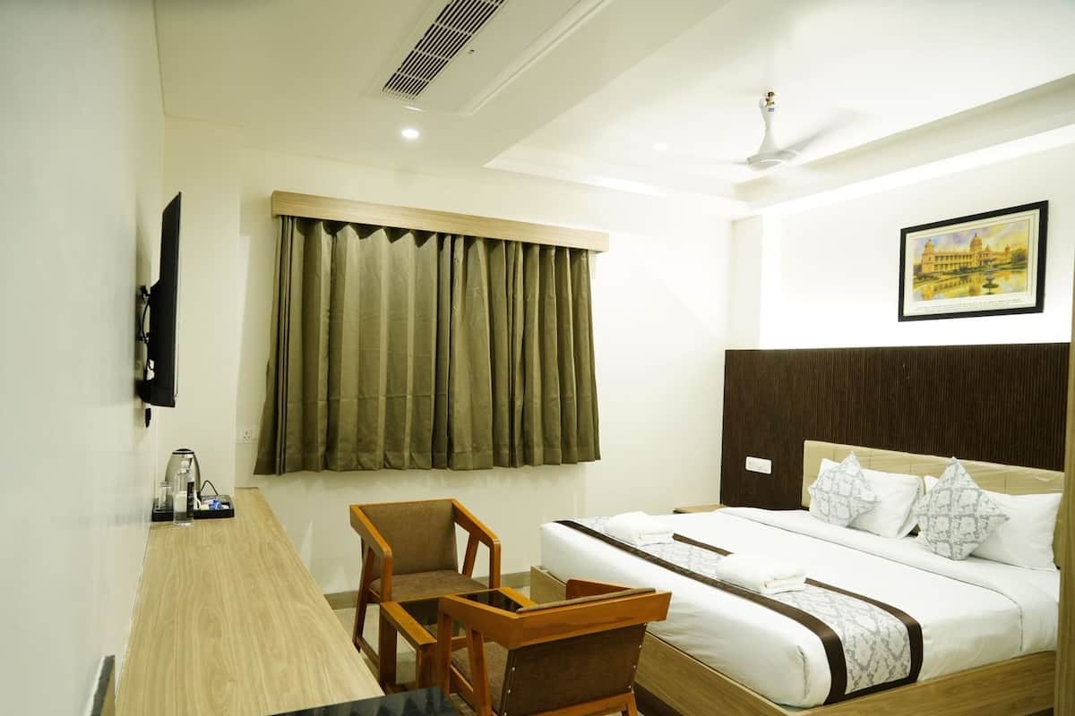 A hotel room with a bed, a desk with a chair, a window with curtains, a ceiling fan, and a framed picture on the wall.