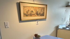 Una pequeña cocina americana con una mesa, dos taburetes, una planta en maceta y una obra de arte enmarcada en la pared.