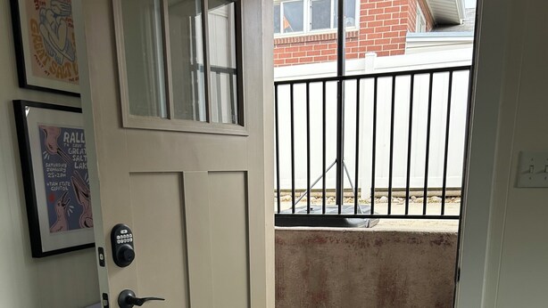 Una puerta con cerradura electrónica, un escalón que da al exterior, una reja metálica y una alfombra estampada en el suelo.
