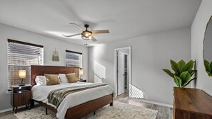 A bedroom with a wooden bed, a ceiling fan, and a large window with blinds. - The Naturehaus - Spacious 4-BR villa with gym/game room in fantastic Bentonville (Bentonville)
