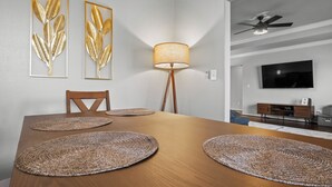 A dining area with a wooden table, four woven placemats, a floor lamp, and two framed leaf artworks on the wall. - The Naturehaus - Spacious 4-BR villa with gym/game room in fantastic Bentonville (Bentonville)