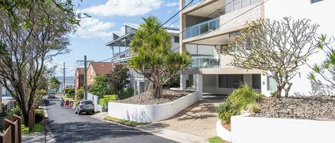 A modern residential street with a two-story house featuring a balcony, a driveway, and a well-maintained garden.