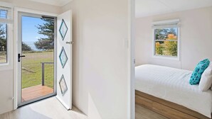 A bedroom with a bed, a window, and a door leading to a balcony. - Marg's - Oceanstays - Oceanfront (Brooms Head)