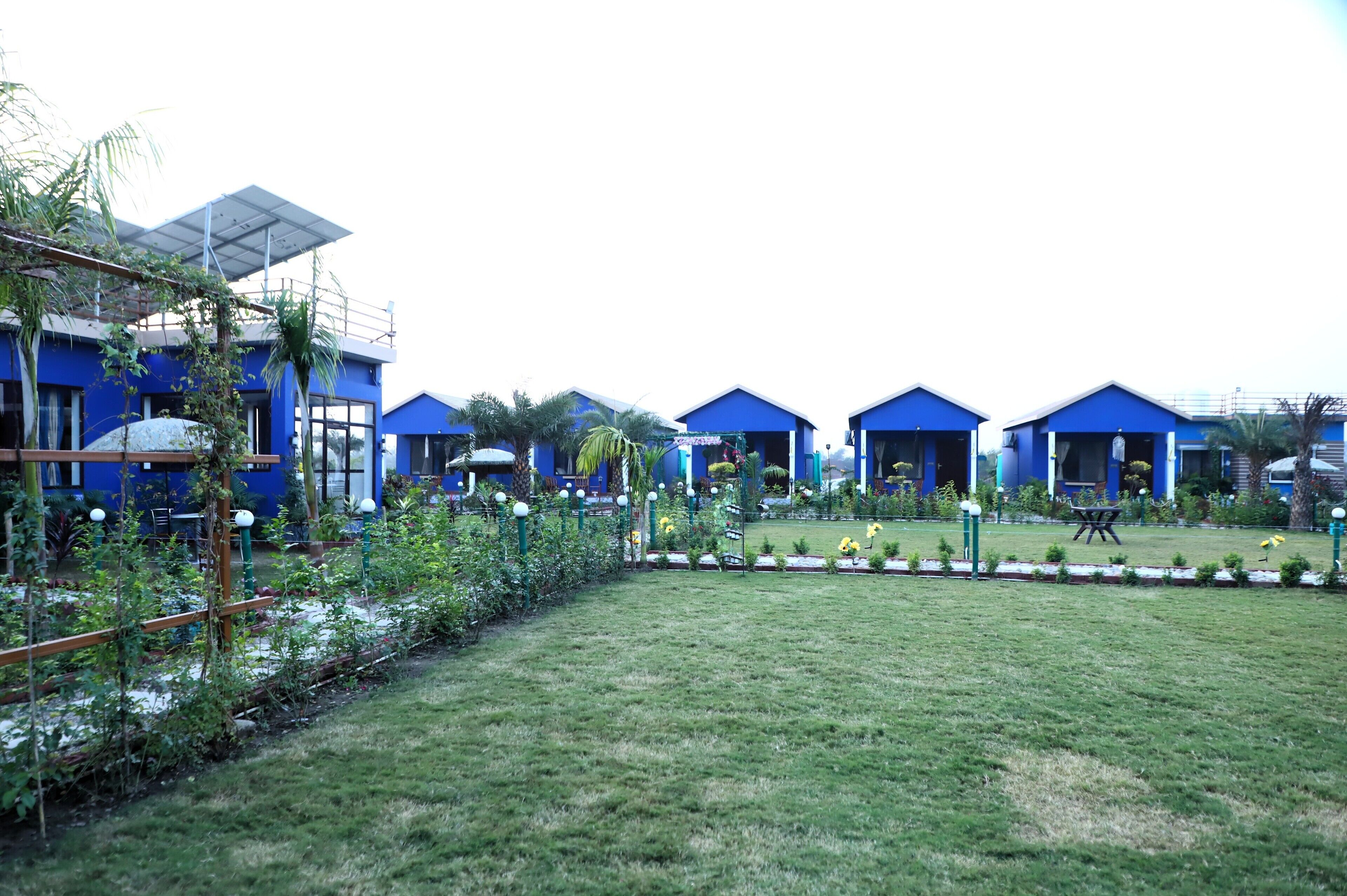 A row of blue-roofed buildings with a grassy lawn and small garden beds in front.