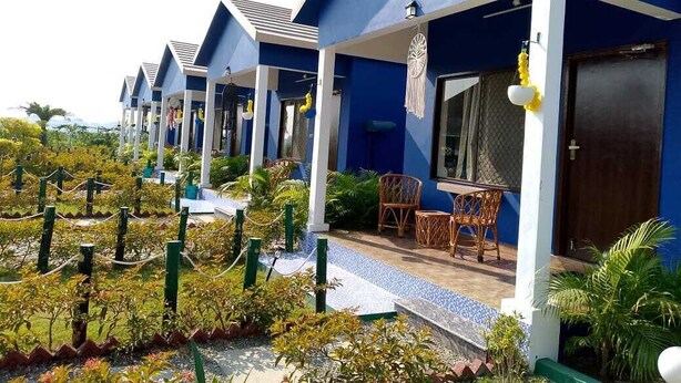 A row of blue buildings with outdoor seating areas and a garden in front. - The Tiger Waterfront Resort (Puranpur)