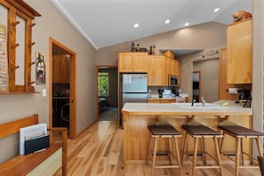 A modern kitchen with wooden cabinets, a central island with stools, a refrigerator, and a microwave. - Salmon's Rest - Rural Riverfront Retreat (Leavenworth)
