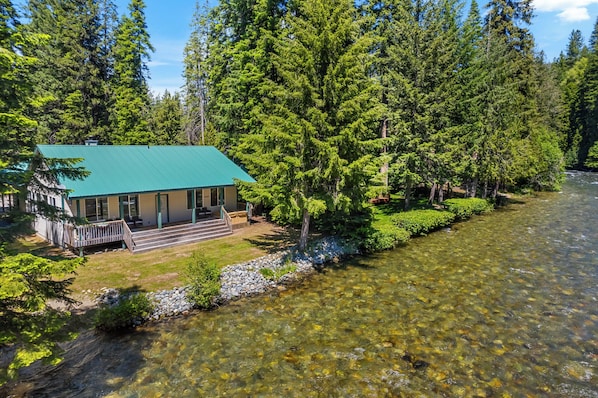 A lodge with a green roof, situated by a clear river, surrounded by dense forest. - Salmon's Rest - Rural Riverfront Retreat (Leavenworth)