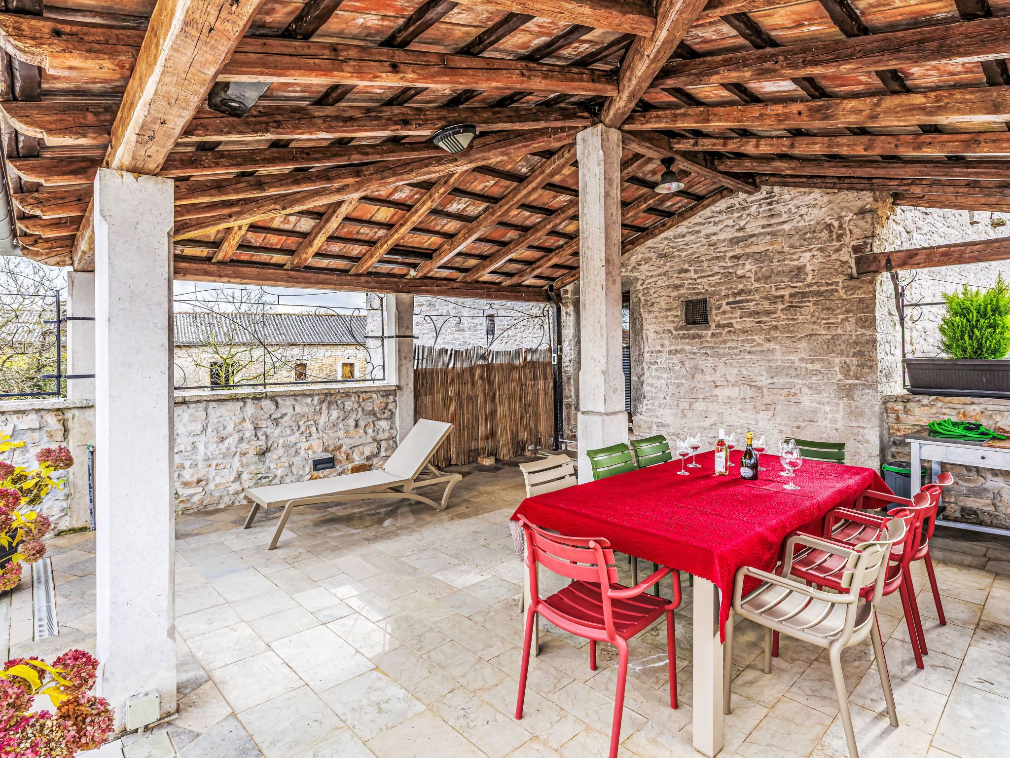 Un área de comedor al aire libre cubierta con pared de piedra, vigas de madera y mantel rojo.