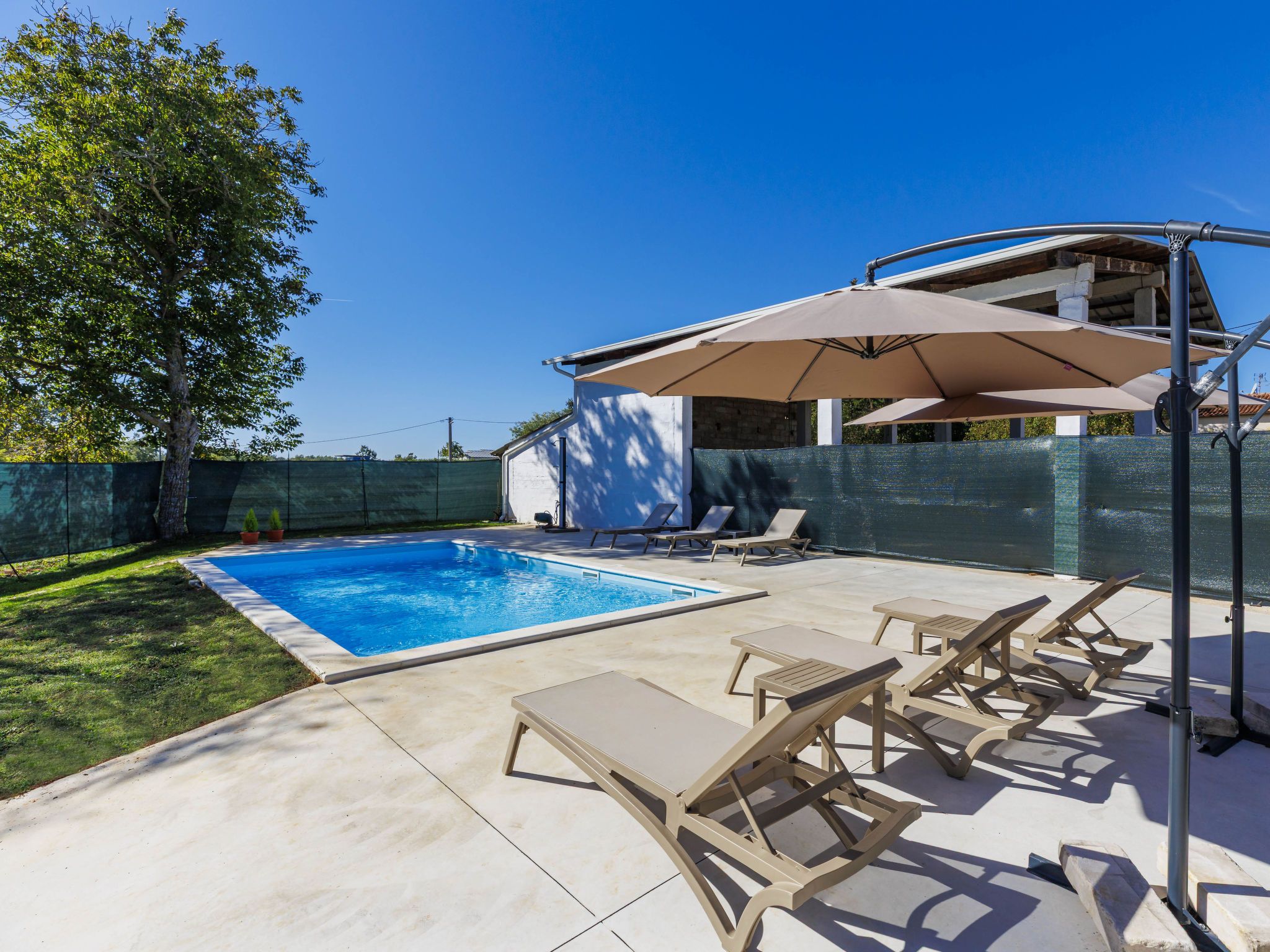 Quintal com piscina, cadeiras de sol e varanda coberta.
