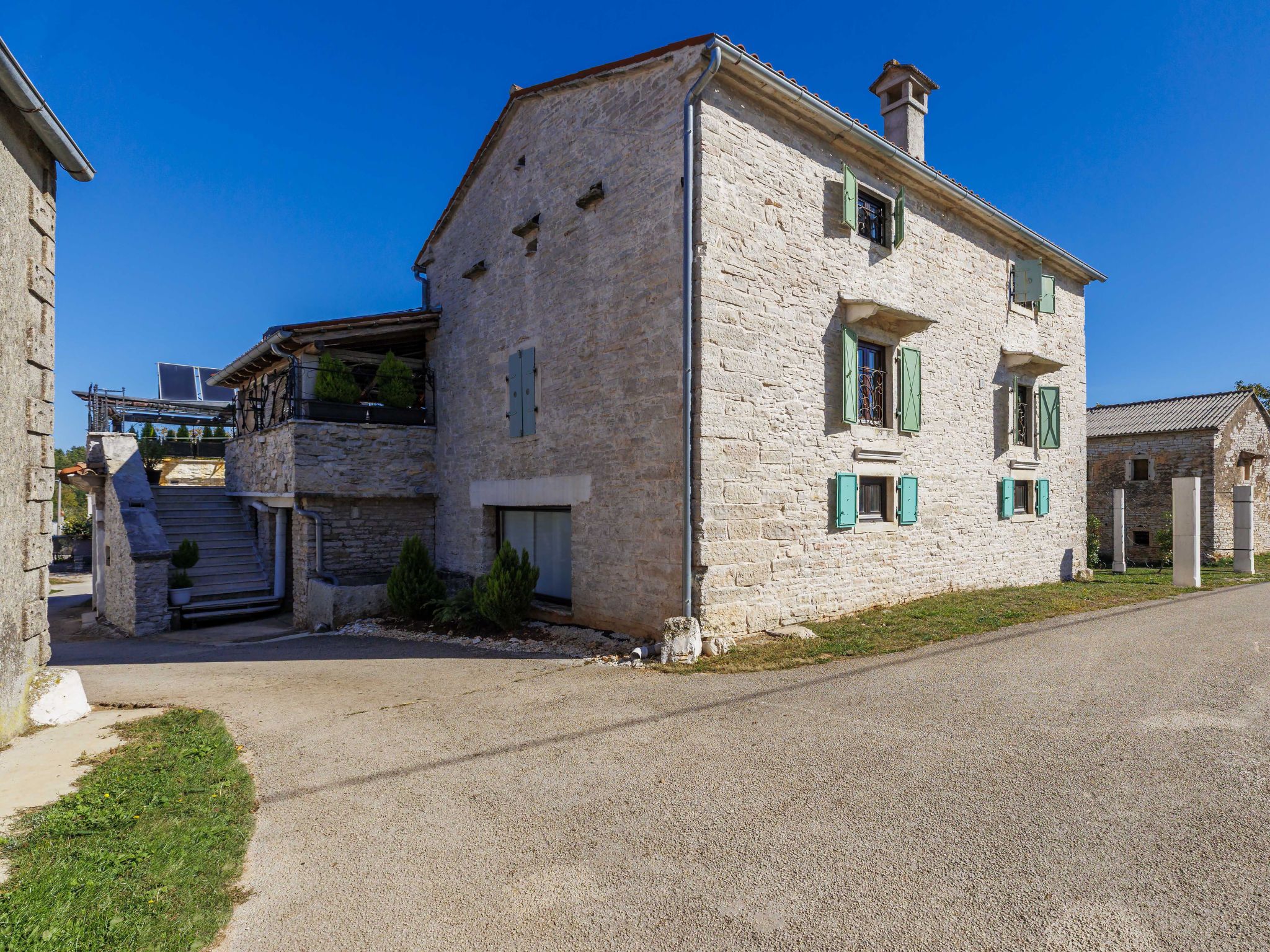 A stone building with a balcony, a small entrance, and a gravel driveway.