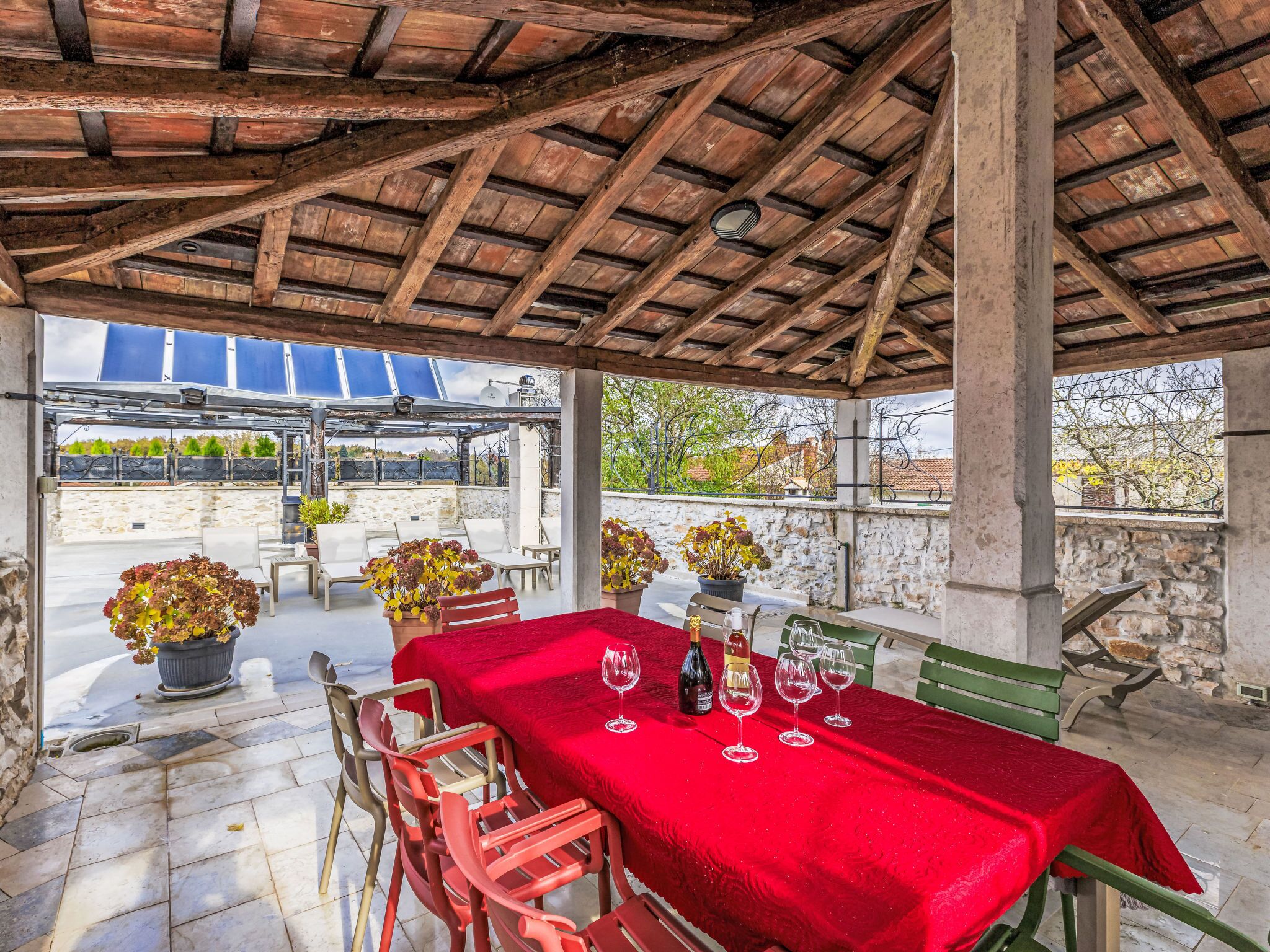 An outdoor patio with a red tablecloth, wine glasses, and chairs.