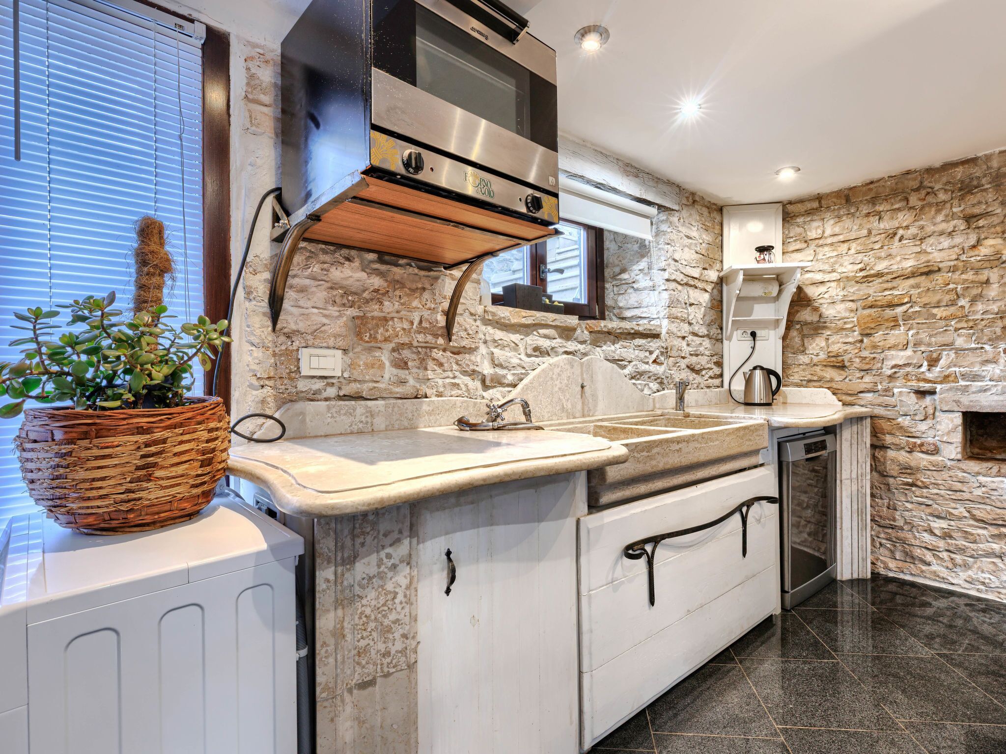 A kitchen with a stone wall, a built-in oven, and a sink.