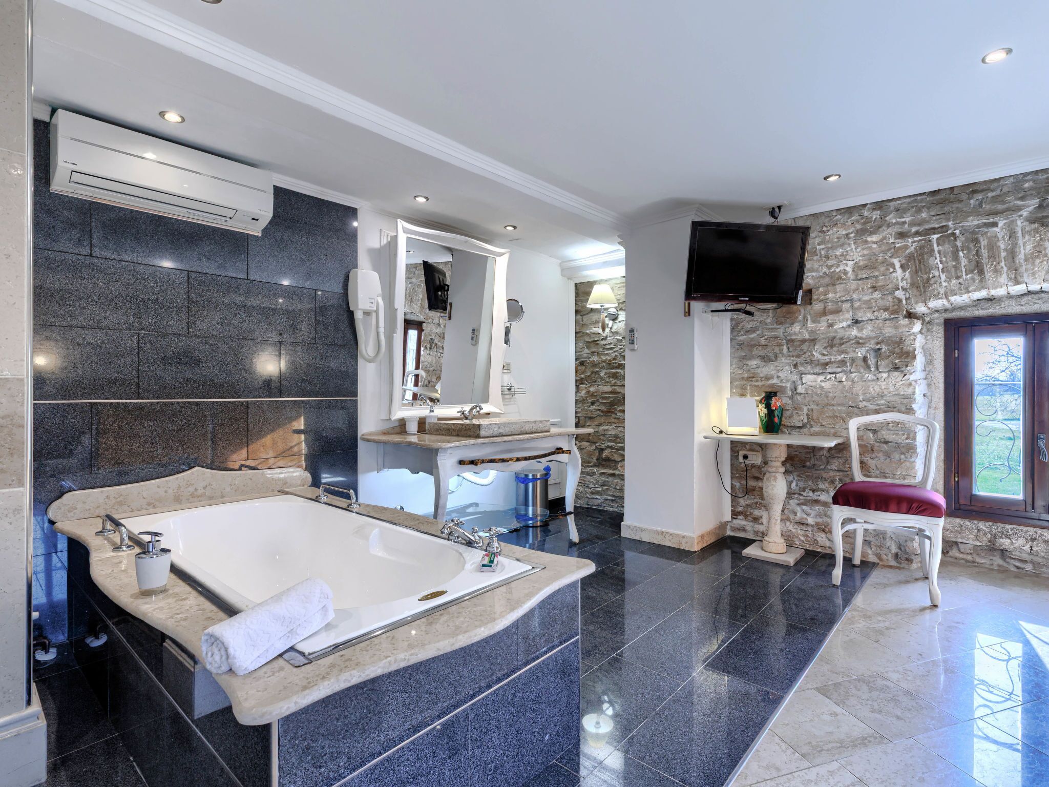 A modern bathroom with a large bathtub, a vanity with a mirror, and a stone wall.