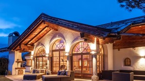 Une maison moderne avec une façade en pierre, de grandes fenêtres en arc de cercle et un patio couvert doté d’un espace salon extérieur.