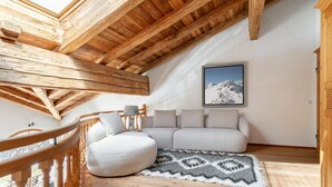 Une chambre mansardée chaleureuse avec un plafond en bois, une grande fenêtre, un canapé et un tapis.