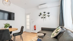 Uma sala de estar moderna com um sofá, uma mesa de jantar com cadeiras, uma TV e um ar condicionado fixado na parede.