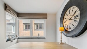 Un comedor con una mesa de madera, dos ventanas con cortinas, un reloj de pared y una lámpara.