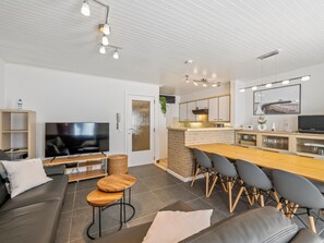 Ein modernes Wohnzimmer mit Flachbildfernseher, einer Couch, einem Esstisch mit Stühlen und einer Küchenzeile inklusive Herd und Schränken.