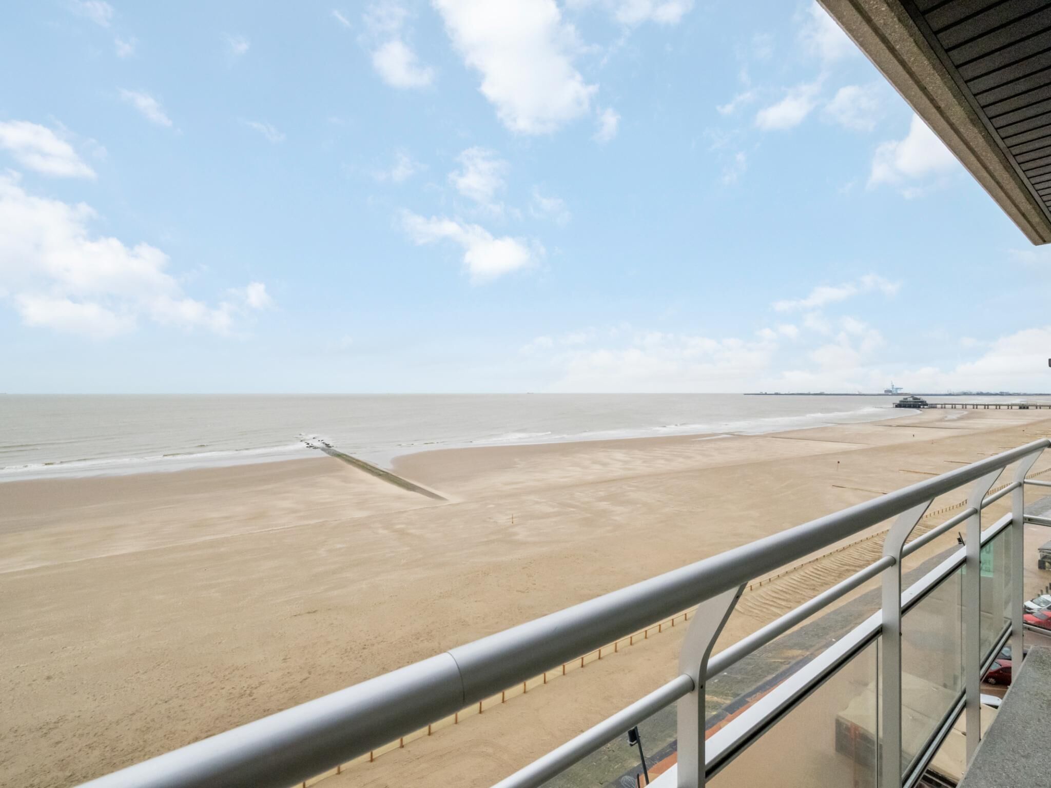 A beach view from a balcony with a metal railing, sandy beach, and a calm sea.
