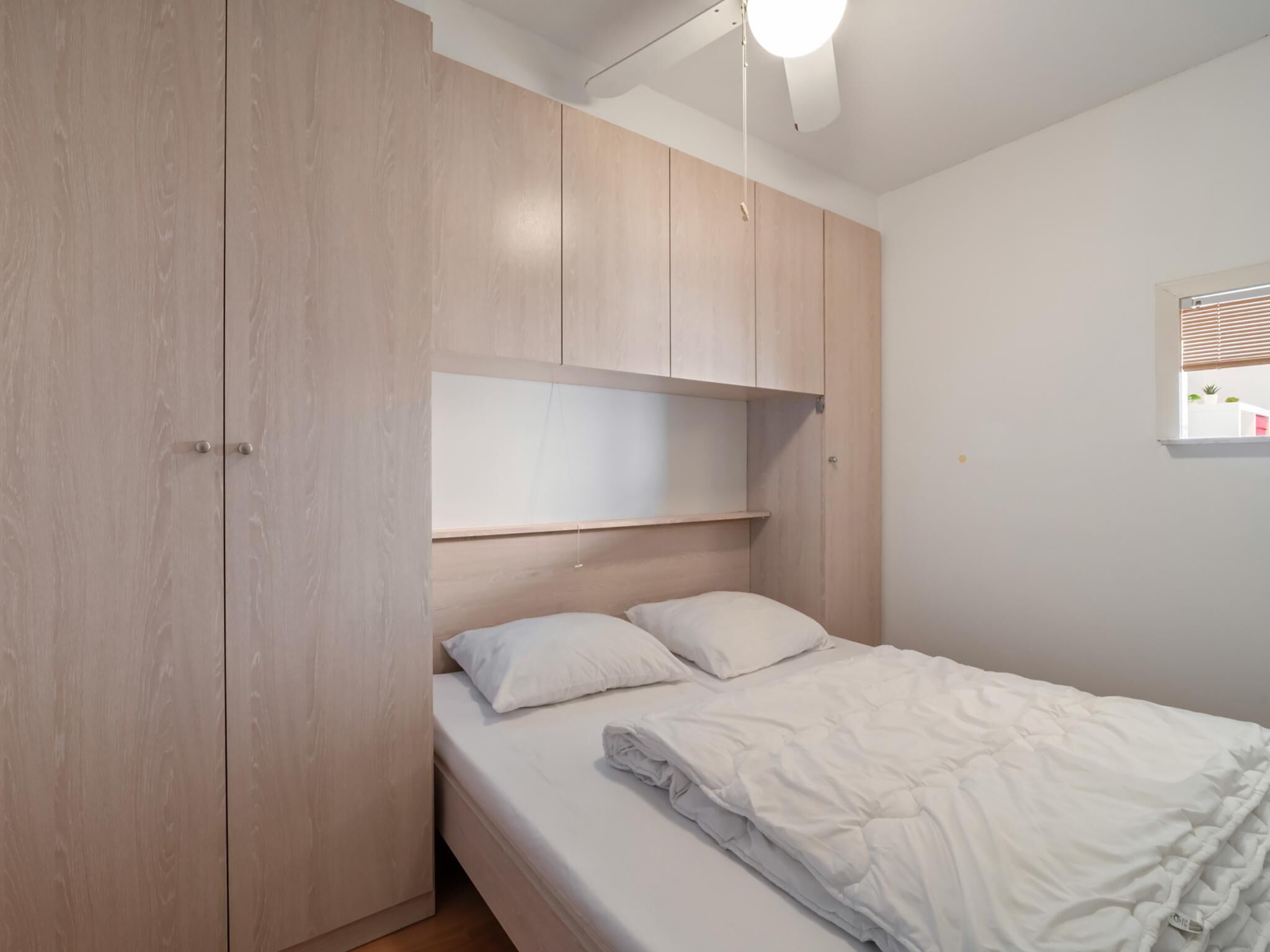 A bedroom with a bed, a wardrobe, and a ceiling fan.