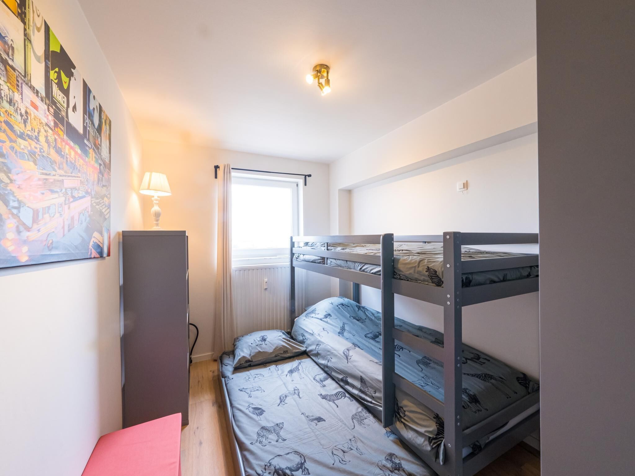 A bunk bed room with a window, a lamp, and a poster on the wall.
