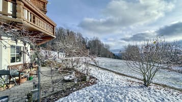 Un jardin enneigé agrémenté d’une pergola en bois et d’un banc en pierre.