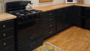 Une cuisine avec un poêle noir, des armoires en bois, un four à micro-ondes et un luminaire fixé au plafond.