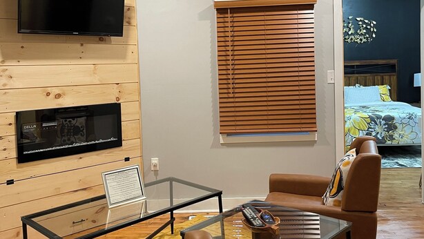 Un salon moderne doté d’un téléviseur à écran plat, d’un ventilateur de plafond, de murs recouverts de panneaux de bois, d’une table basse en verre et d’un canapé en cuir marron.