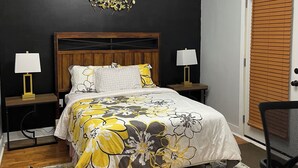 Une chambre à coucher comprenant un lit, des tables de chevet, un bureau, une chaise, une porte avec des stores et un luminaire au plafond.