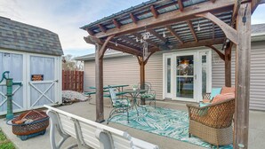 Un patio cubierto con una pérgola de madera, muebles de exterior y una alfombra decorativa.