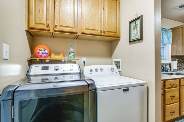 A laundry area with a front-loading washer and dryer, wooden cabinets above, and a framed schedule on the wall.
