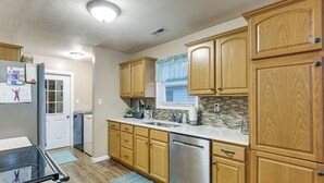Una cocina con armarios de madera, lavavajillas de acero inoxidable y una ventana con cortina azul.