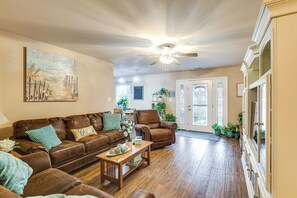 A spacious living room with a brown leather sofa, a wooden coffee table, and a ceiling fan.