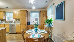 Una cocina con armarios de madera, lavavajillas, una mesa de comedor con platos azules y servilletas blancas, y una araña.