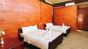 Habitación de hotel con dos camas, paredes de paneles de madera, suelo de madera y una mesita con un jarrón de flores.