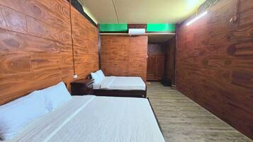 A room with two beds, wooden walls, a green accent wall, and a ceiling light.