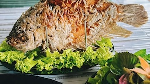 Un pescado entero asado, sobre un plato con lechuga y hierbas.