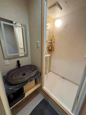 A bathroom with a round sink, a mirror, a shower, and a small shelf with toiletries. - SUN WARM HOUSE (Osaka)