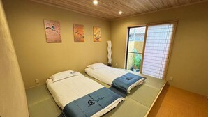 A room with two beds, tatami mats, a wooden ceiling, and a sliding door to a balcony. - SUN WARM HOUSE (Osaka)
