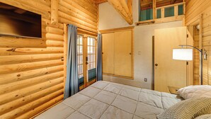 Una habitación tipo cabaña de madera con una cama, un televisor, un armario y una ventana con cortinas.